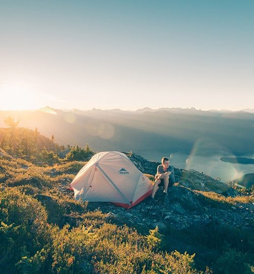 Person sitting by a tent at sunset.