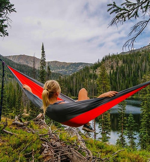 Person relaxing in hammock among trees.
