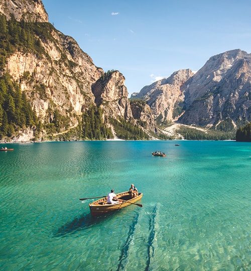 Boaters on calm turquoise lake surrounded by mountains.