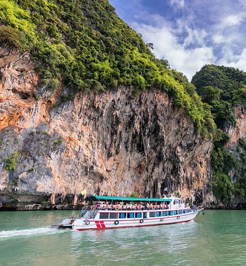 Boat cruising past lush rocky cliffs.